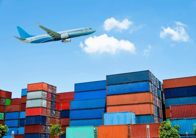 A plane flying over many different coloured stacked shipping containers.